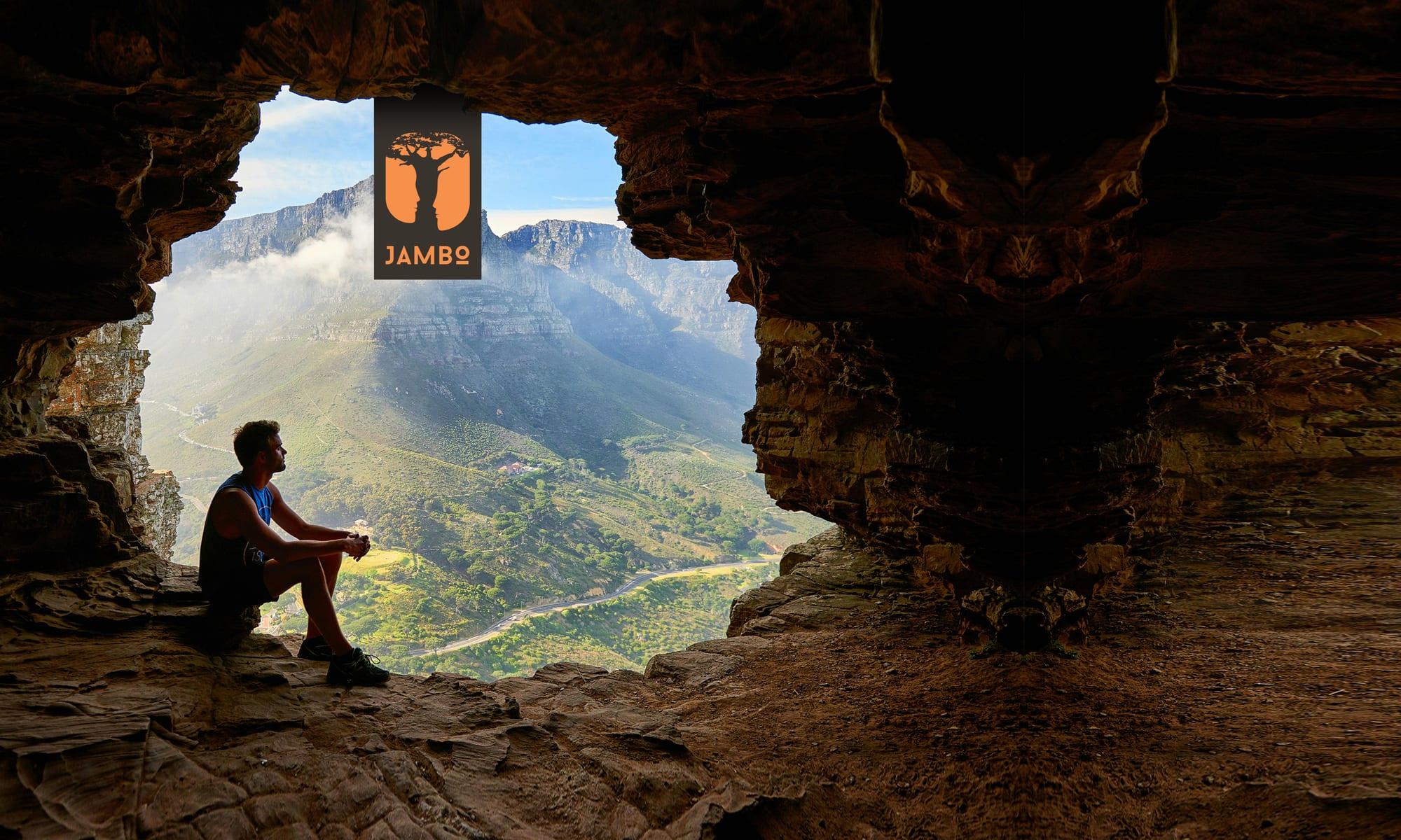 Hiker resting at a cave mouth above a green mountain valley, with the Jambo logo